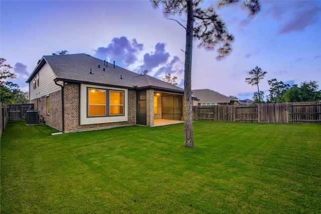back of house at dusk featuring a fenced backyard, a patio area, a yard, and brick siding