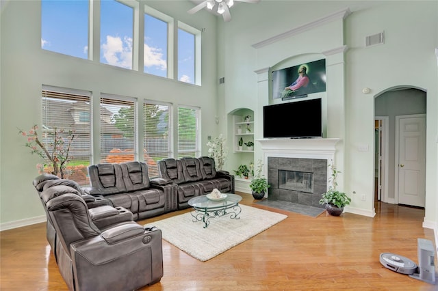 living area with a towering ceiling, arched walkways, built in shelves, a tile fireplace, and a ceiling fan