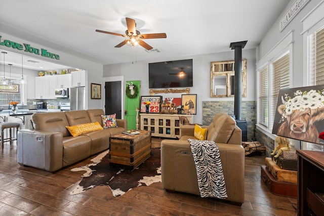 living area featuring dark wood-style flooring, a ceiling fan, visible vents, and a wood stove