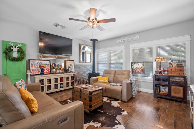 living room featuring visible vents, a wood stove, wood finished floors, baseboards, and a ceiling fan