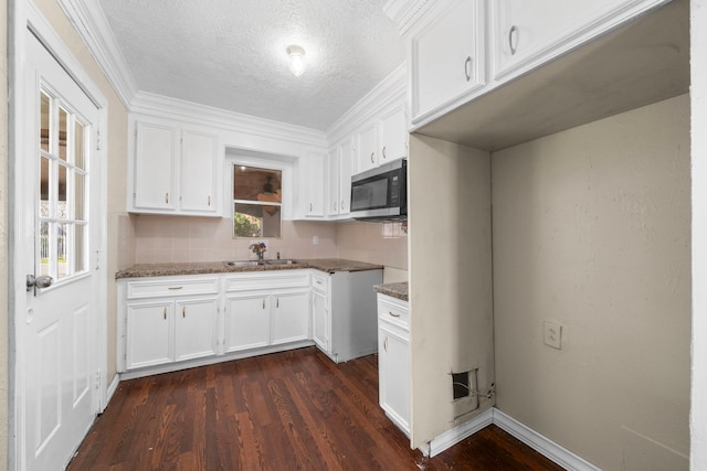 kitchen with a sink, a textured ceiling, white cabinetry, stainless steel microwave, and dark wood-type flooring