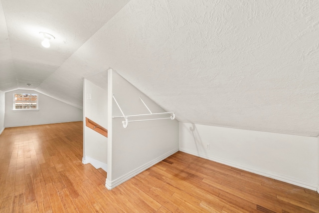 additional living space featuring baseboards, a textured ceiling, vaulted ceiling, and light wood-style flooring