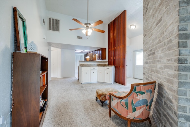 sitting room with ceiling fan, visible vents, light carpet, and a high ceiling
