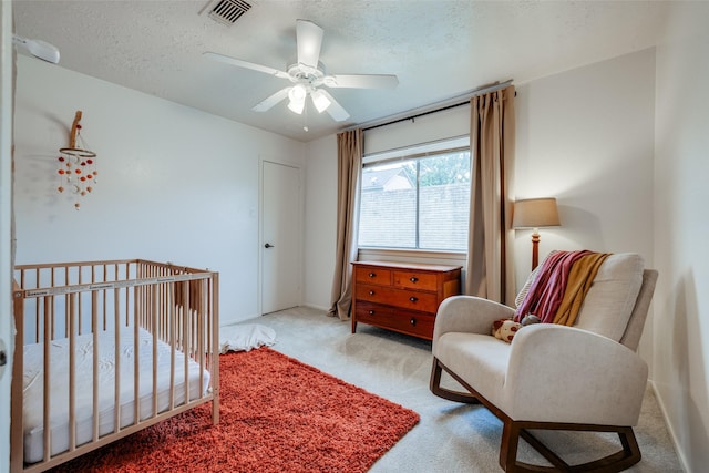 bedroom with a ceiling fan, a textured ceiling, visible vents, carpet floors, and a crib