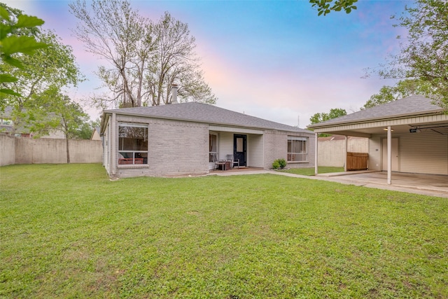 back of property at dusk with brick siding, a patio area, fence, and a yard