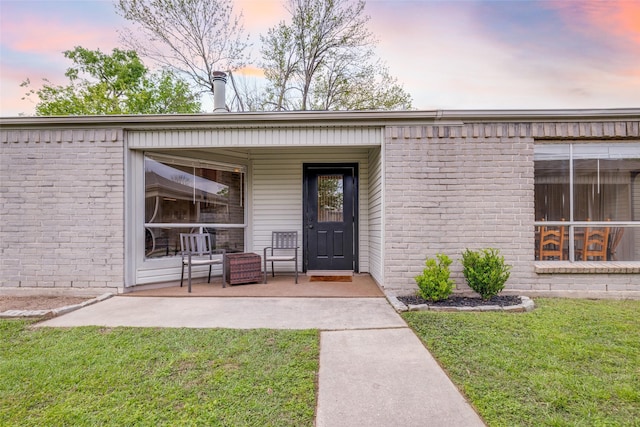 entrance to property featuring a lawn, covered porch, and brick siding