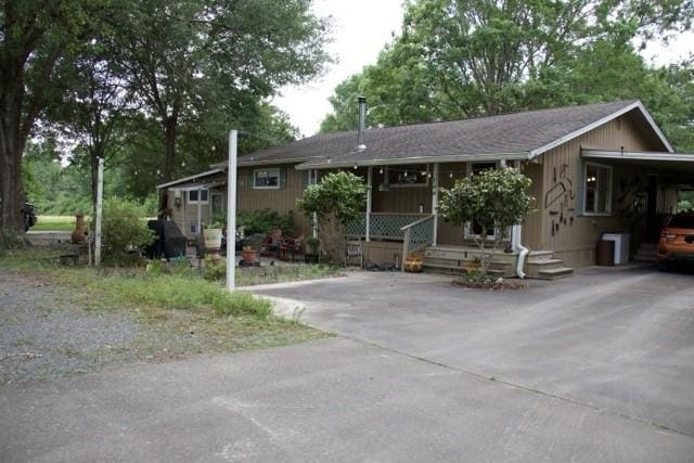 single story home featuring a porch, driveway, roof with shingles, and a carport