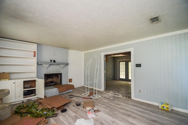 living area with a brick fireplace, a textured ceiling, baseboards, wood finished floors, and visible vents