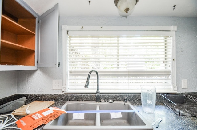 kitchen featuring a sink, dark countertops, and a textured wall
