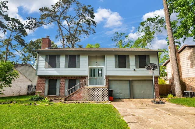 raised ranch featuring central AC, a chimney, brick siding, an attached garage, and driveway