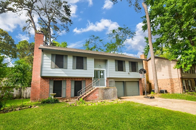 bi-level home featuring driveway, a chimney, a front yard, brick siding, and an attached garage