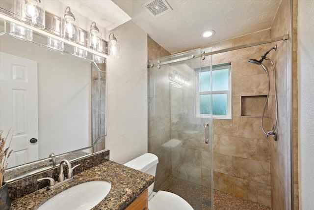 bathroom featuring visible vents, vanity, a textured wall, toilet, and a stall shower