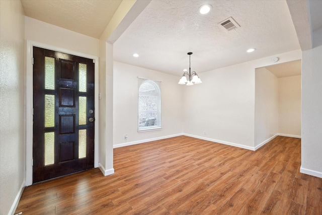 entryway with an inviting chandelier, light wood-style floors, baseboards, and visible vents