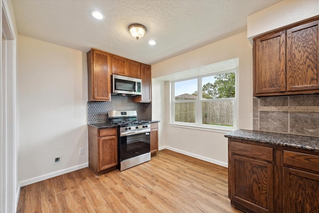 kitchen featuring baseboards, appliances with stainless steel finishes, light wood finished floors, and tasteful backsplash