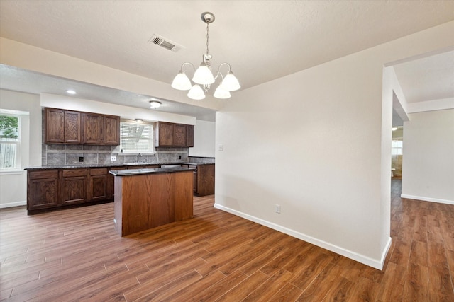 kitchen featuring a chandelier, baseboards, wood finished floors, a kitchen island, and visible vents