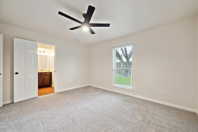 unfurnished bedroom with a ceiling fan, visible vents, light colored carpet, baseboards, and ensuite bathroom