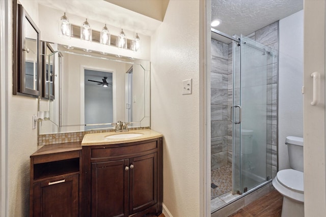 bathroom featuring a textured wall, vanity, toilet, a ceiling fan, and a stall shower