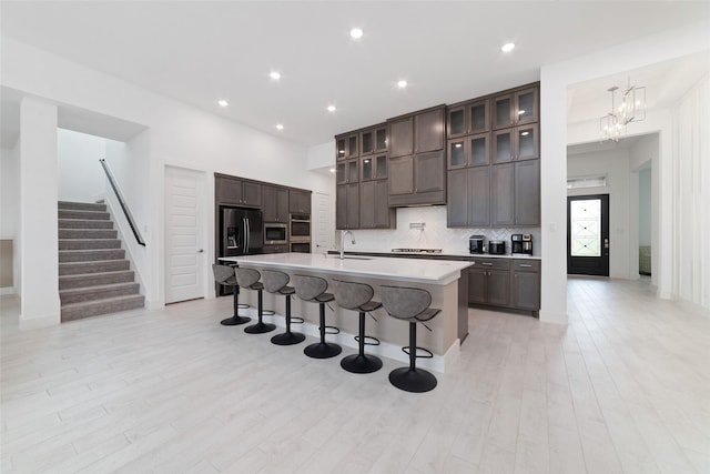 kitchen featuring dark brown cabinetry, a breakfast bar area, tasteful backsplash, a sink, and stainless steel appliances