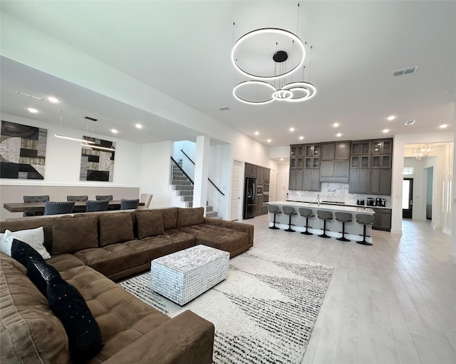 living area featuring light wood finished floors, a chandelier, recessed lighting, visible vents, and stairway