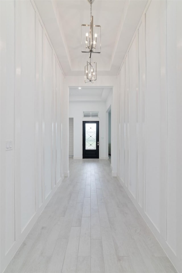 hallway with a tray ceiling, a notable chandelier, and a decorative wall