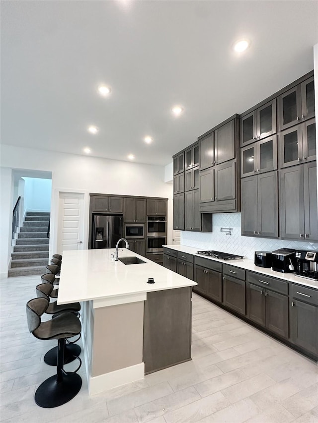 kitchen with a kitchen island with sink, appliances with stainless steel finishes, tasteful backsplash, a sink, and light countertops