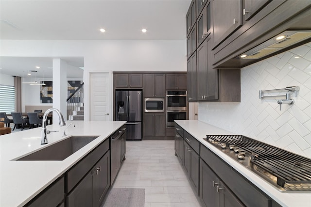 kitchen featuring light countertops, under cabinet range hood, tasteful backsplash, a sink, and appliances with stainless steel finishes