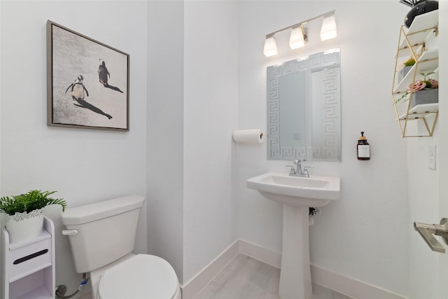 half bathroom with a sink, baseboards, toilet, and wood finished floors
