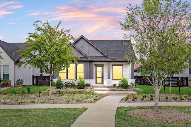 view of front of home featuring a shingled roof, board and batten siding, fence, and a yard