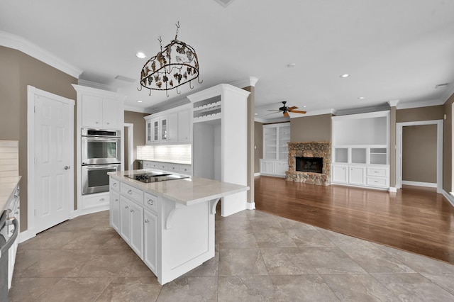 19731 Stone Lake Dr, Tomball, TX 77377 - kitchen featuring double oven, a ceiling fan, crown molding, white cabinets, and a fireplace