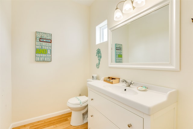 half bath with vanity, baseboards, wood finished floors, and toilet