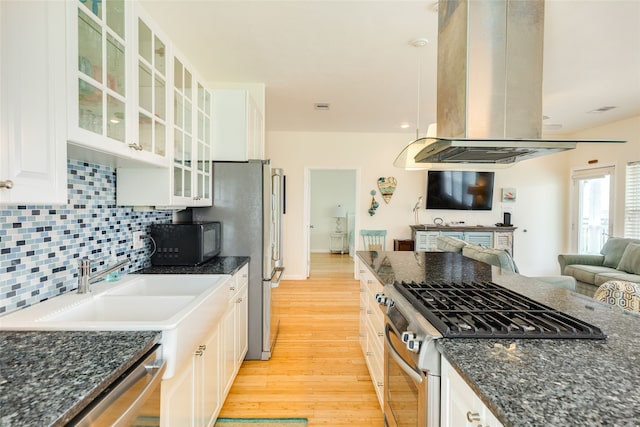 kitchen featuring open floor plan, island range hood, light wood finished floors, backsplash, and stainless steel appliances
