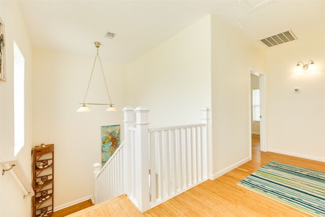 hall with baseboards, an upstairs landing, wood finished floors, and visible vents