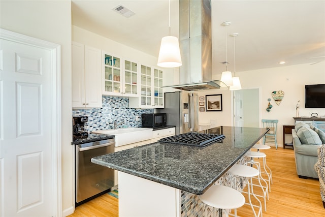 kitchen featuring a breakfast bar area, island range hood, appliances with stainless steel finishes, light wood-type flooring, and a sink