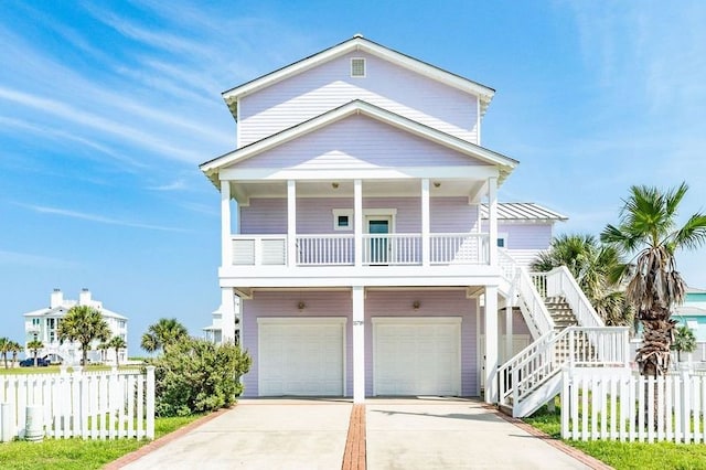 beach home featuring fence, stairs, a garage, concrete driveway, and covered porch