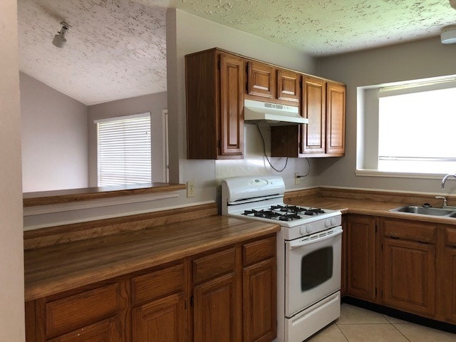 kitchen with white gas range, brown cabinetry, a textured ceiling, a sink, and under cabinet range hood