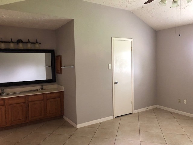 bathroom with double vanity, baseboards, ceiling fan, tile patterned floors, and vaulted ceiling