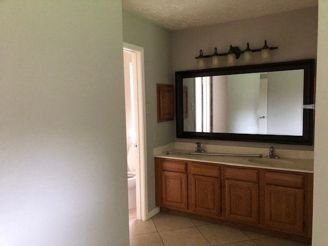 bathroom featuring double vanity, a sink, tile patterned floors, and toilet