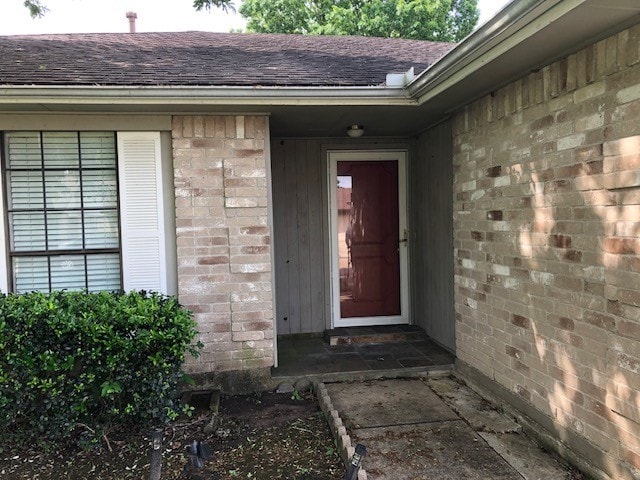 entrance to property with roof with shingles and brick siding