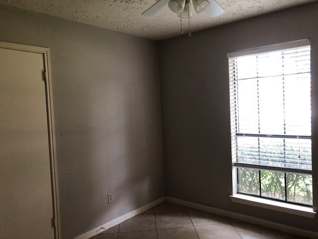 tiled empty room featuring baseboards, a ceiling fan, and a textured ceiling