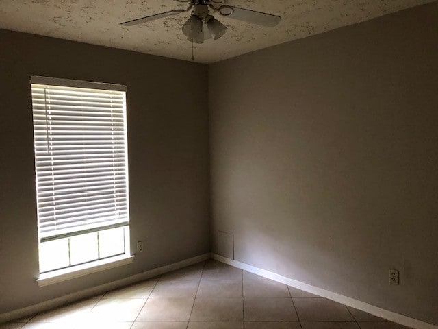 tiled empty room with baseboards and a ceiling fan