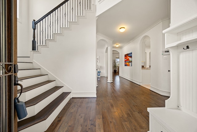 entrance foyer with crown molding, dark wood-style flooring, stairs, baseboards, and arched walkways