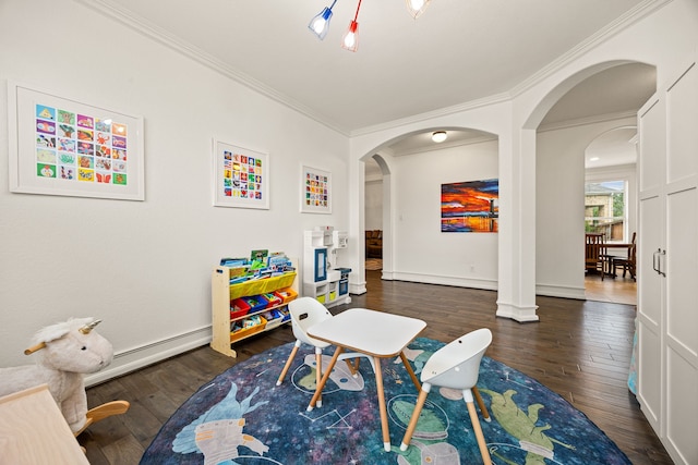 playroom featuring dark wood-type flooring, ornamental molding, arched walkways, and a baseboard heating unit