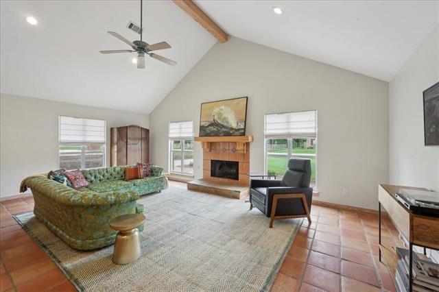 tiled living area with beam ceiling, high vaulted ceiling, a tiled fireplace, a ceiling fan, and visible vents