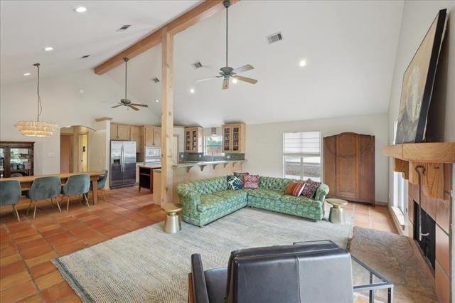 living room featuring a tiled fireplace, beam ceiling, high vaulted ceiling, ceiling fan with notable chandelier, and light tile patterned flooring