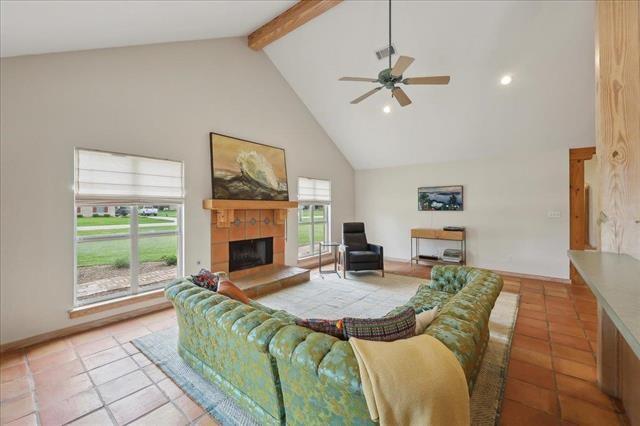 living area with beam ceiling, a fireplace, ceiling fan, high vaulted ceiling, and light tile patterned floors
