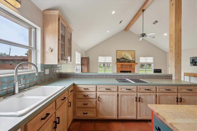 kitchen featuring lofted ceiling with beams, black electric stovetop, a sink, light brown cabinets, and a ceiling fan