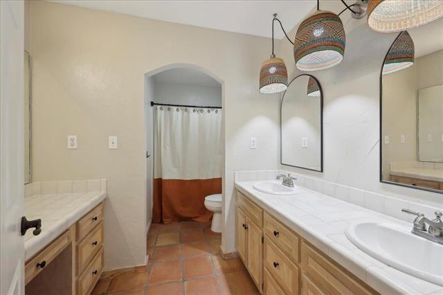 bathroom featuring double vanity, a sink, curtained shower, and toilet