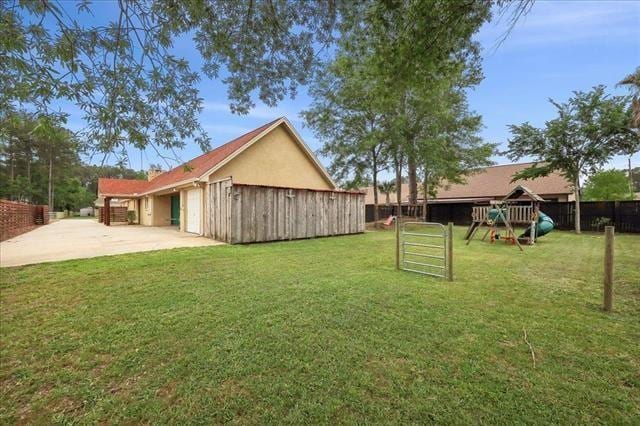 view of yard with a garage, fence, a patio area, a playground, and driveway