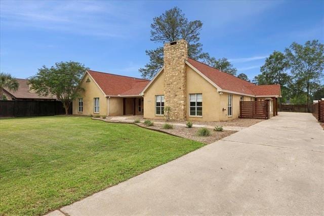 rear view of property with a chimney, a lawn, fence, concrete driveway, and stucco siding