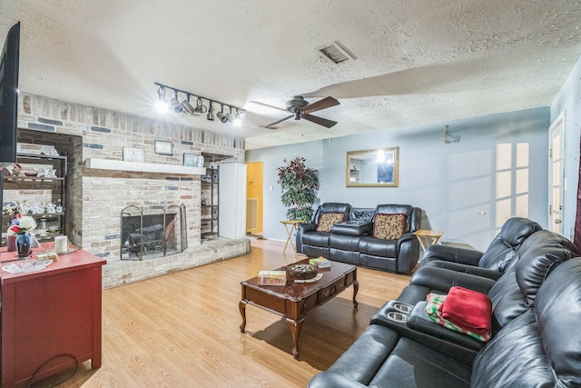 living room with a fireplace, a textured ceiling, a ceiling fan, wood finished floors, and visible vents